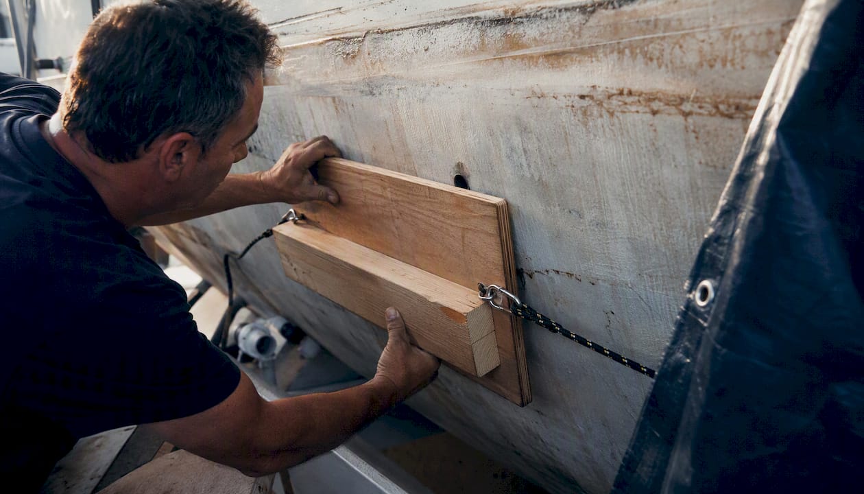 Hands bracing plywood patch on hull leak