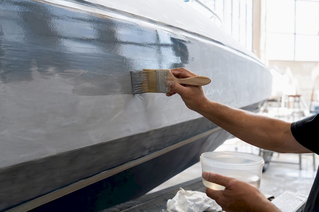 Hands applying epoxy barrier coat on yacht hull