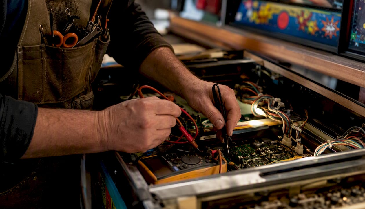 Hands testing arcade machine electrical components with multimeter