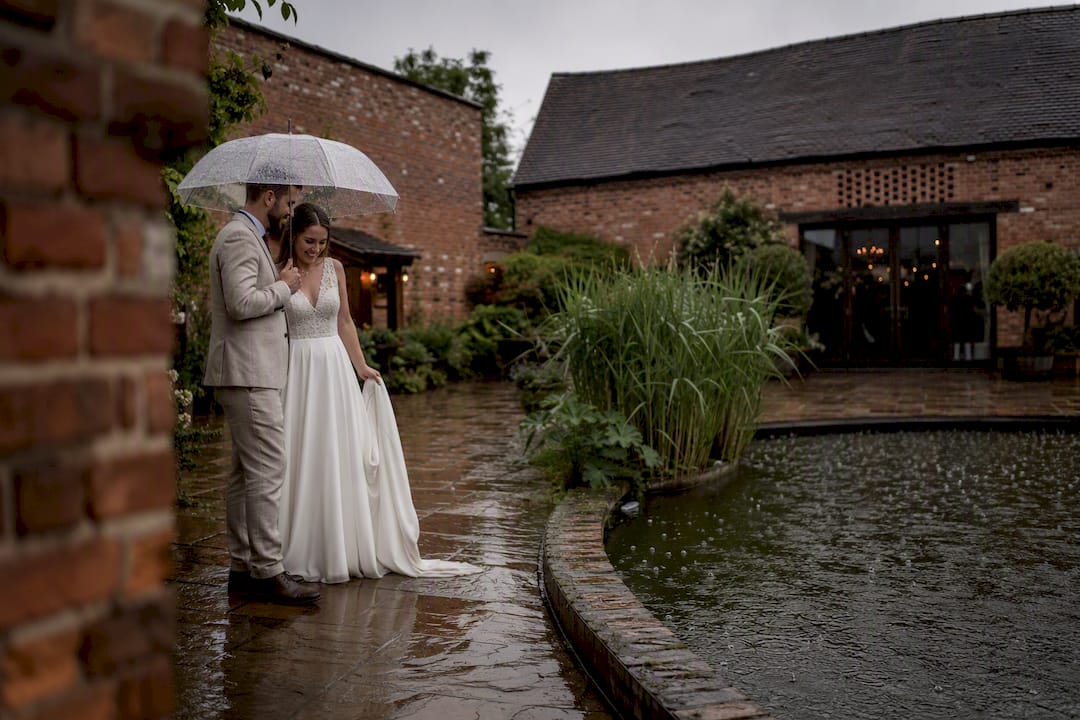 Wedding couple under umbrellas in Shustoke Barn courtyard