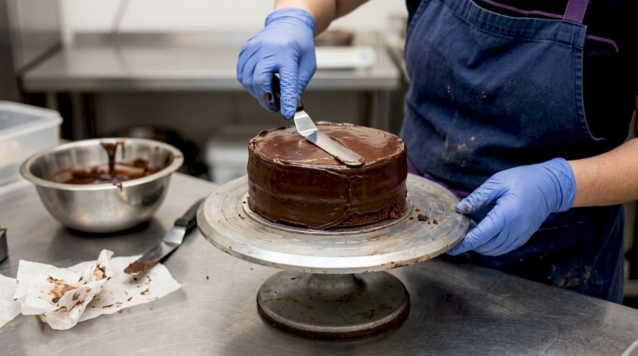 Hands applying ganache crumb coat on cake