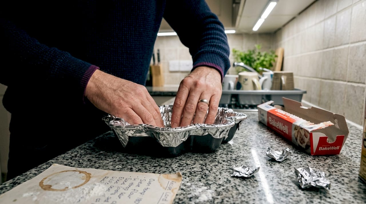 Hands lining tin with foil in kitchen
