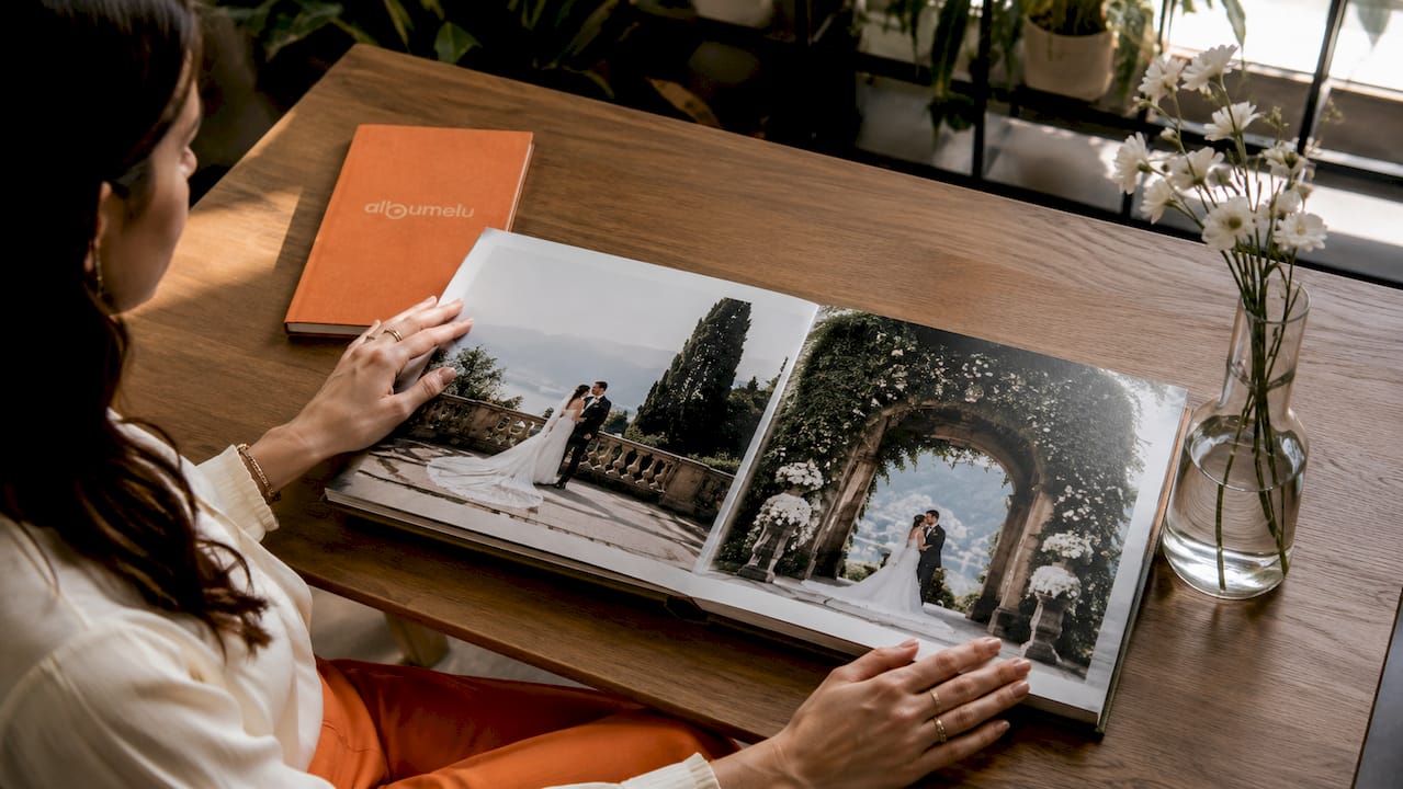 Mâini care răsfoiesc un album de nuntă elegant, cu pagini ce se așază perfect plat și fotografii așezate într-o ordine cronologică, spunând povestea zilei pas cu pas.