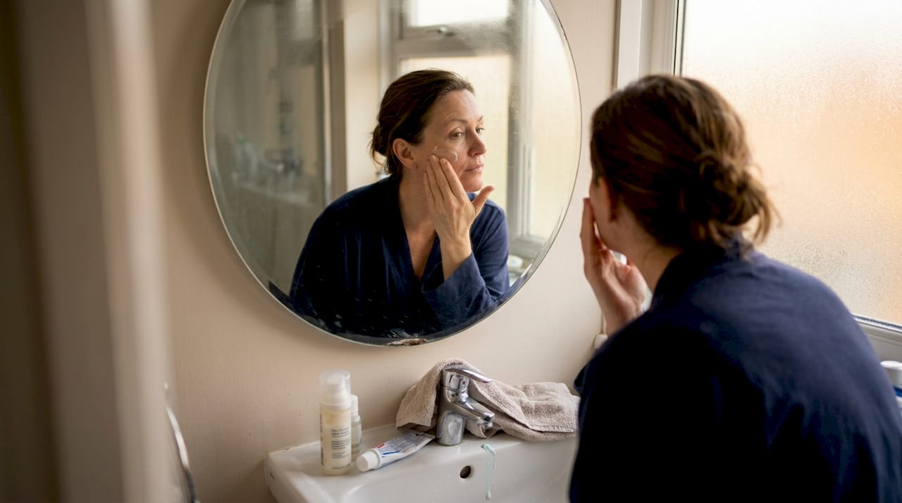 Woman applying moisturizer in realistic bathroom setting