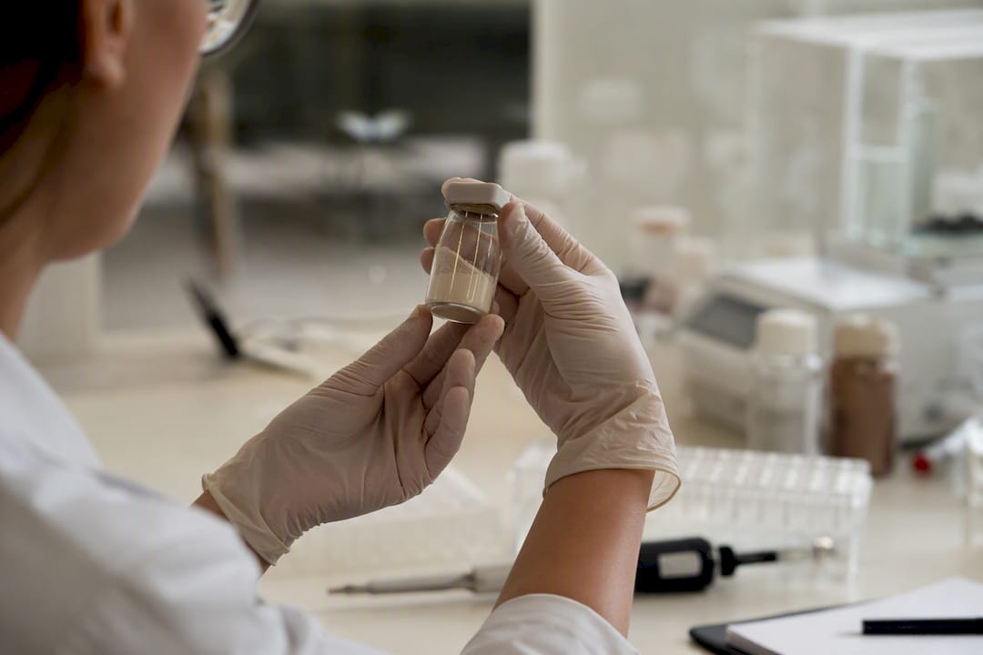 Gloved hands holding supplement batch sample vial