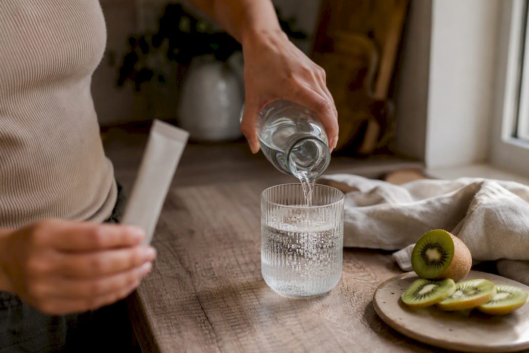 Hands preparing collagen drink on kitchen counter