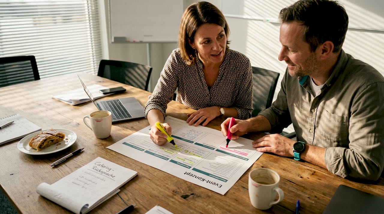 Das Team wirft gemeinsam einen Blick auf die ausgedruckte Vorlage für die Veranstaltung und bespricht Details.