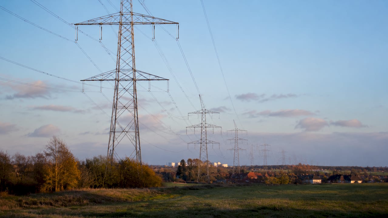 Een hoogspanningsmast die zich uitstrekt over het landschap, terwijl de zon langzaam achter de horizon verdwijnt.