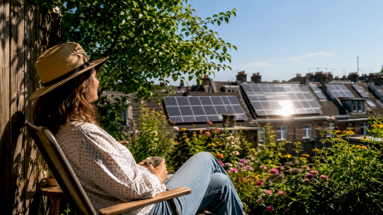 Vanaf haar balkon kijkt een vrouw uit over de stad, waar overal zonnepanelen op de daken liggen.