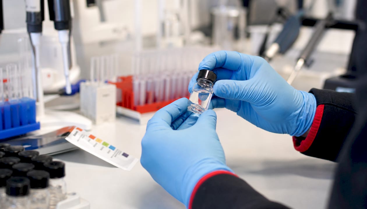 Gloved hands holding sample vial in lab