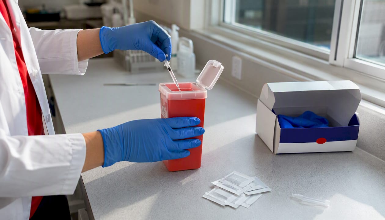 Gloved hands dispose needle safely