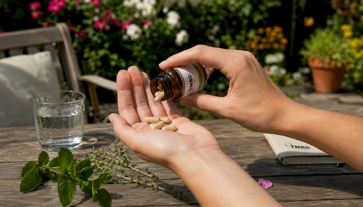Hand holding herbal vocal supplement capsules surrounded by natural ingredients