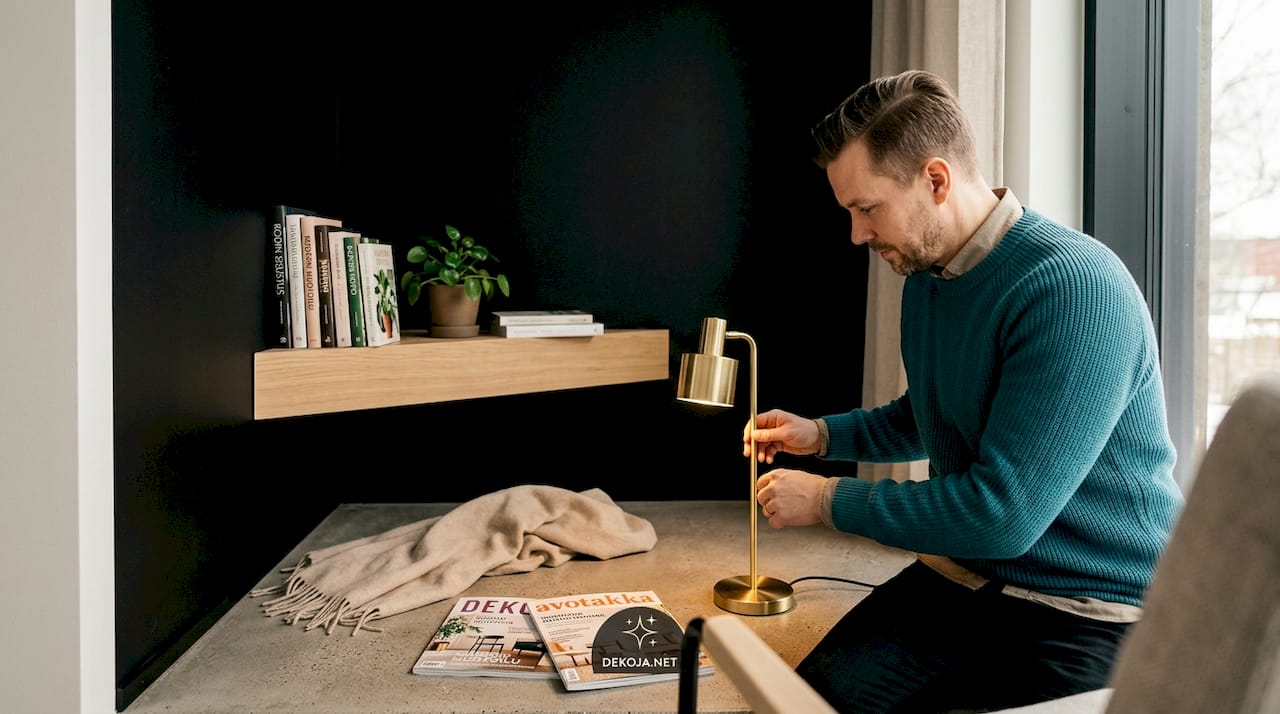 Henkilö istuu rauhallisessa nurkkauksessa, jossa on mattamusta seinä ja tunnelmallinen valaisin.