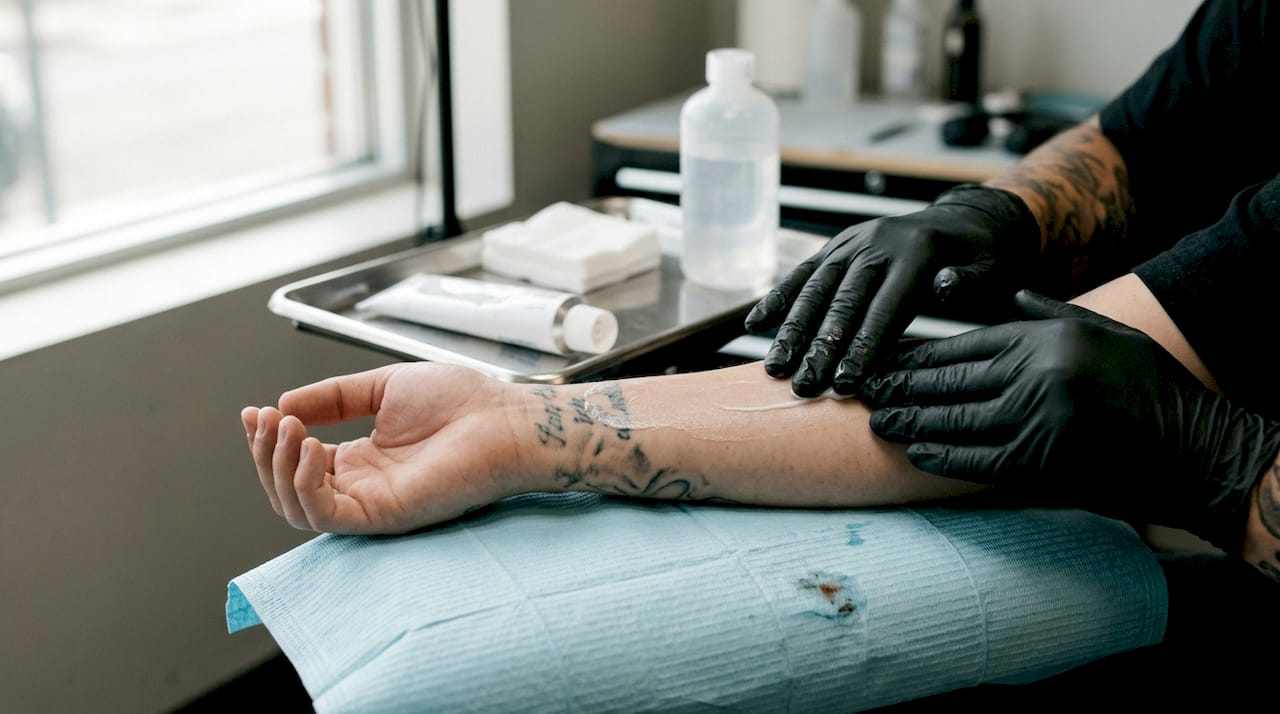 Une personne portant des gants étale une crème anesthésiante sur l’avant-bras.