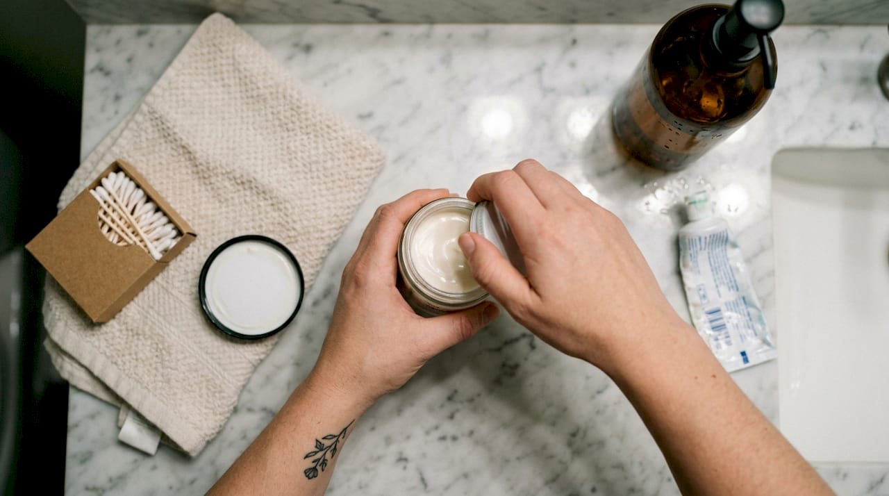 Ein Paar Hände öffnet vorsichtig eine Dose mit veganer Tattoo-Pflege.