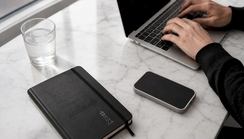 Des mains s’activent sur un clavier, accompagnées d’un carnet de croquis à portée de main.