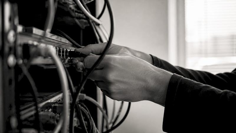 Des mains connectent un câble Ethernet à un switch réseau.