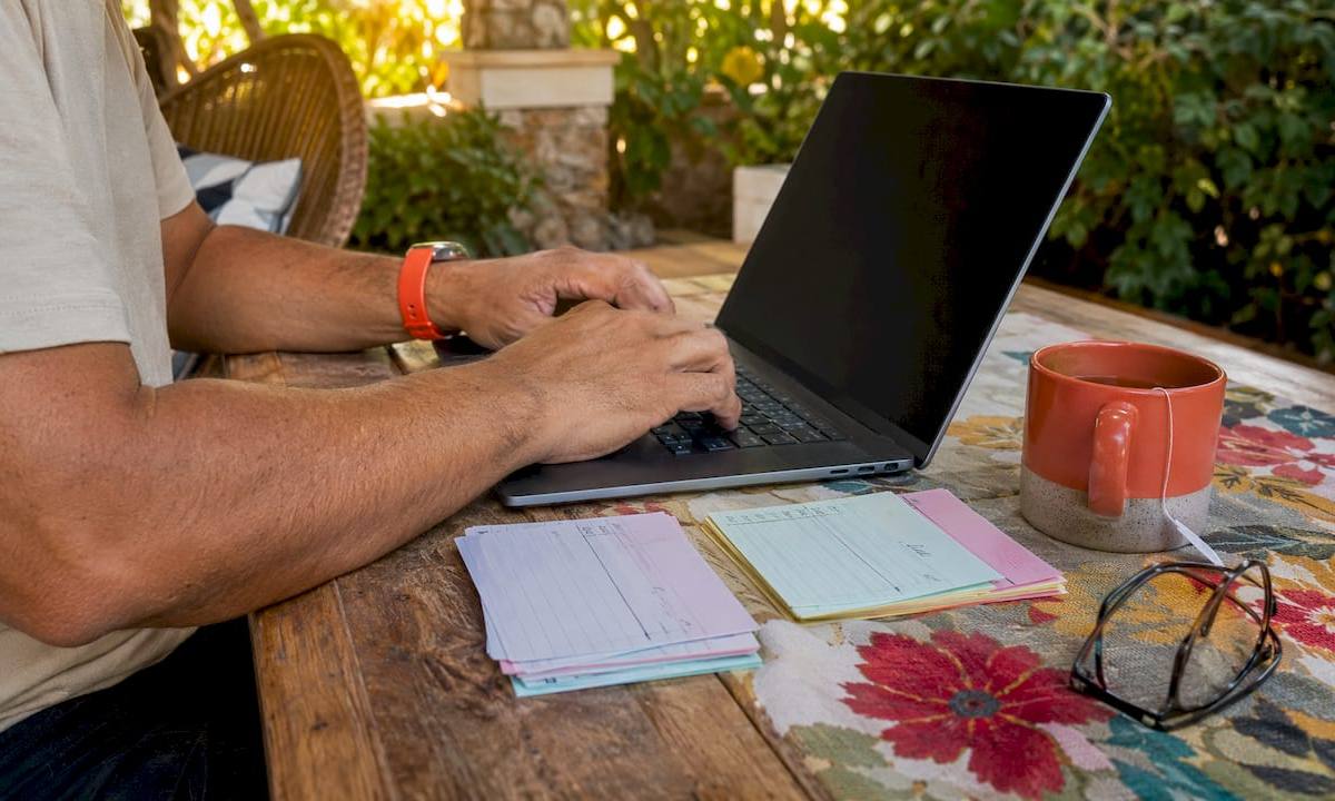 Hands typing on laptop with service scores paperwork