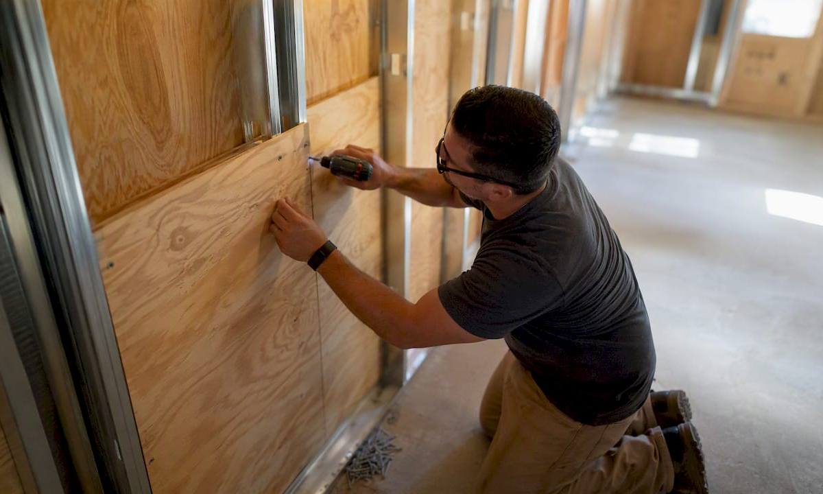 Hands fastening plywood backer to metal studs