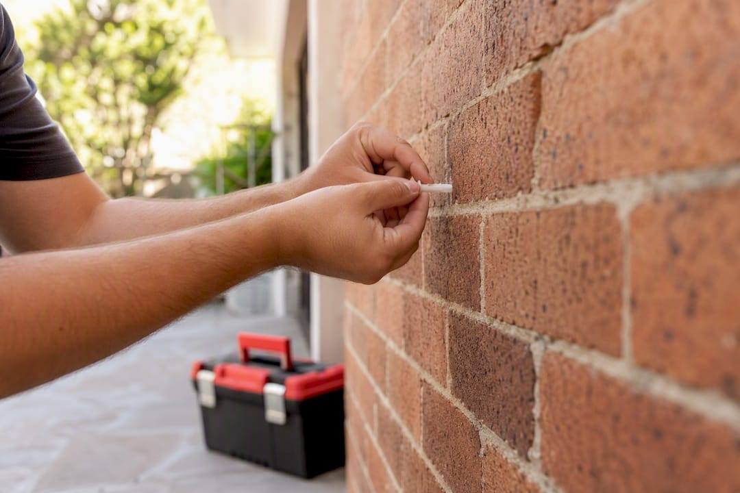 Hands inserting masonry anchor into brick hole
